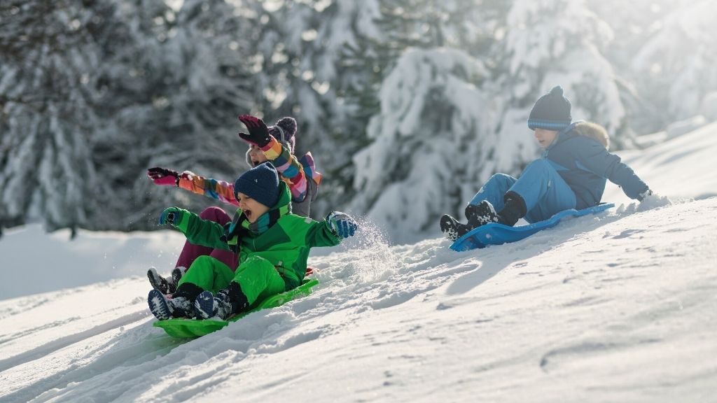 Bilden föreställer tre barn som åker ner för en snötäckt backe i varsin pulka.