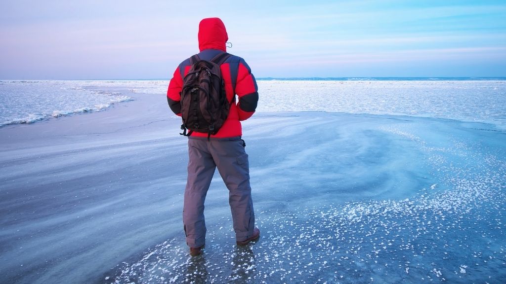 Bilden föreställer en man, iförd vinterkläder, som står mitt ute på en is. Han är vänd bort från kameran.