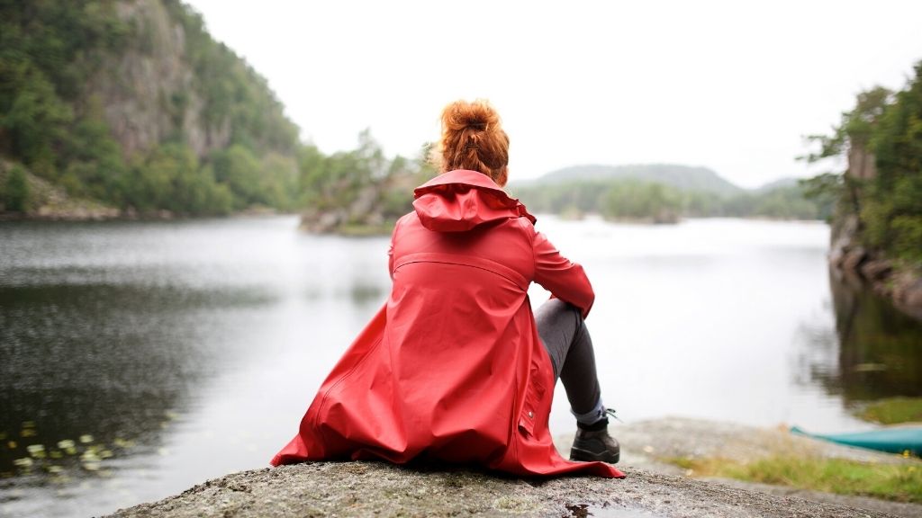 Bilden föreställer en kvinna som sitter på en berghäll och blickar ut över en sjö. Hon sitter med ryggen mot kameran. Kvinnan har rött hår och bär en röd regnjacka.